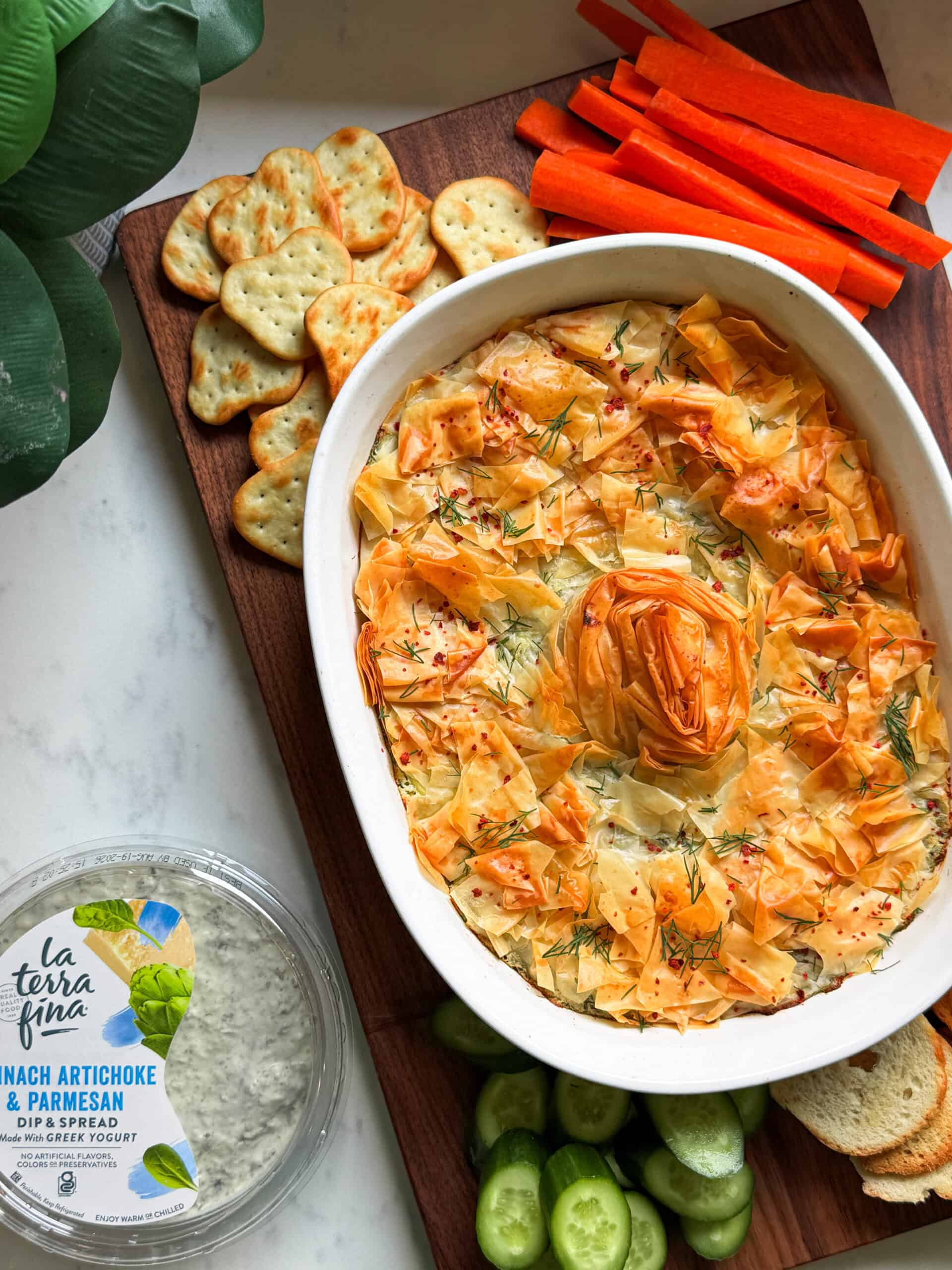 Baked spanakopita dip with a golden phyllo spiral, served with crackers and vegetables