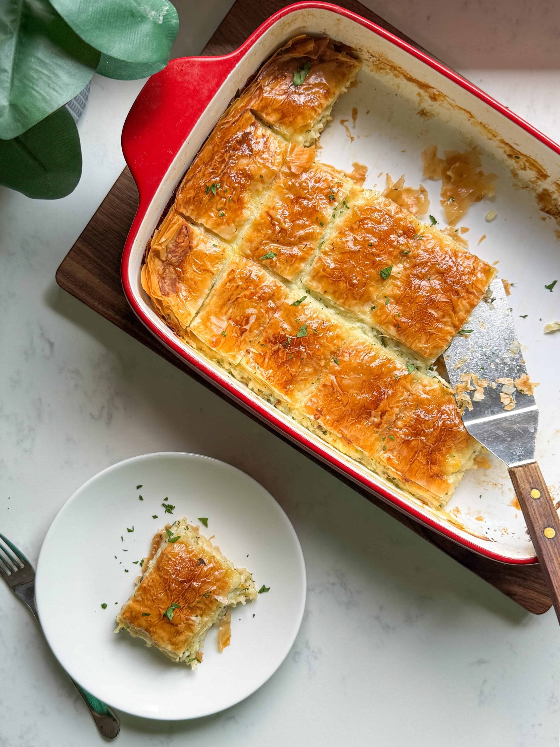 Slicing a piece of Armenian cheese borek from the baking dish with a spatula
