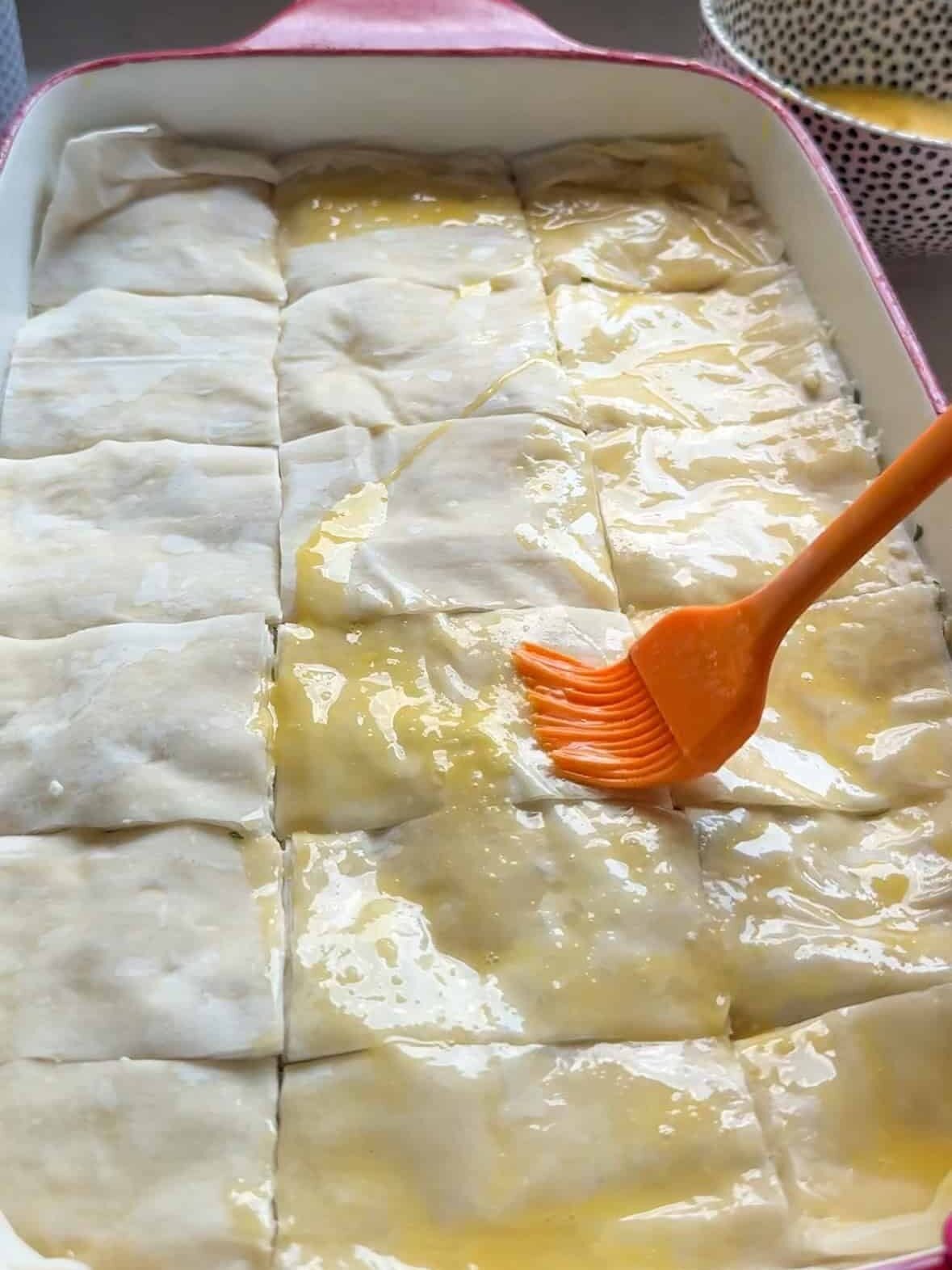 Egg wash being brushed over scored phyllo dough before baking Armenian cheese boreg