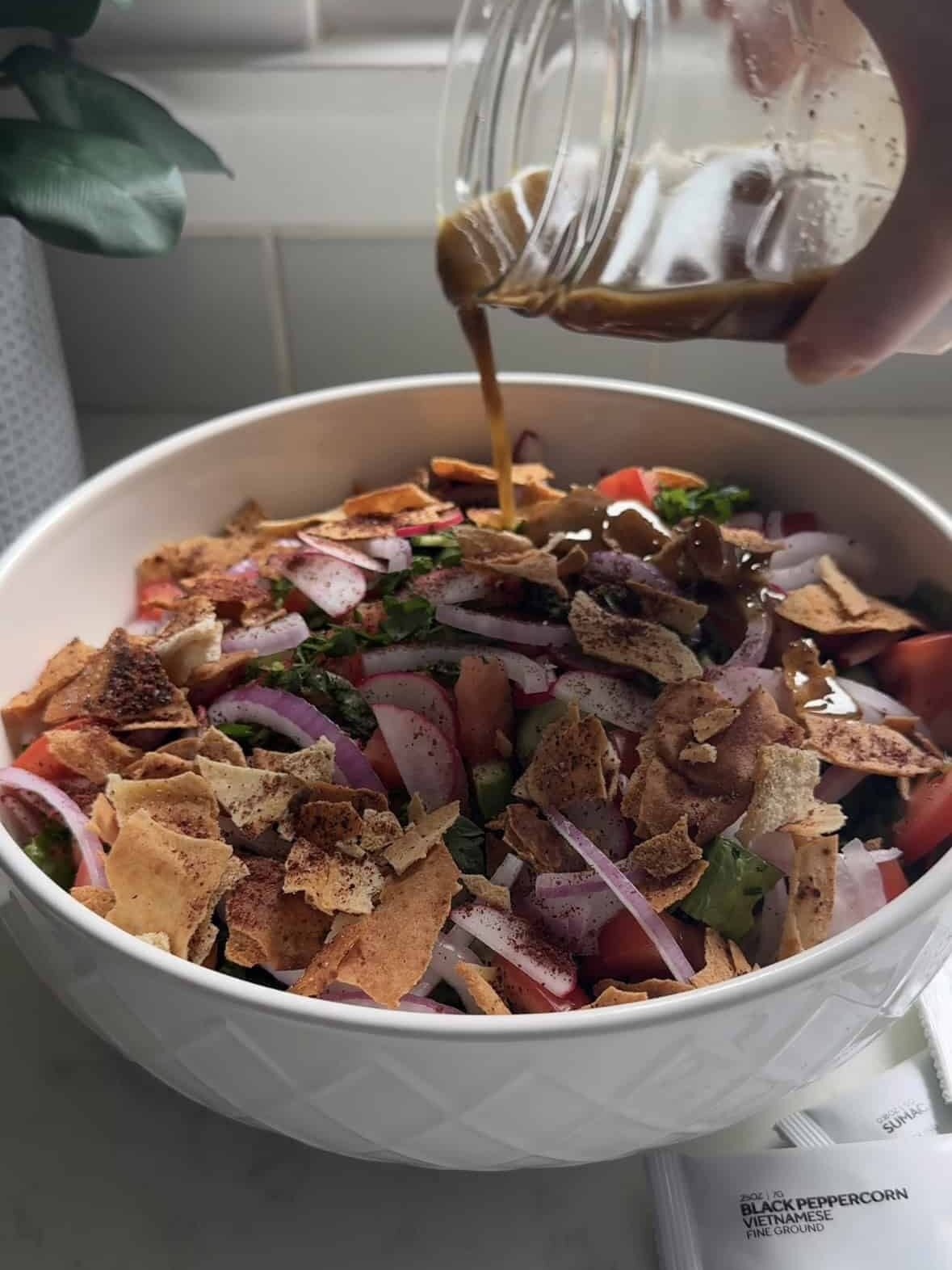 Pouring fattoush dressing over a bowl of chopped vegetables and toasted pita