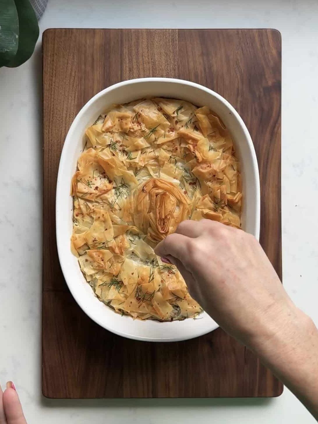 Adjusting the golden phyllo spiral on a freshly baked spanakopita dip