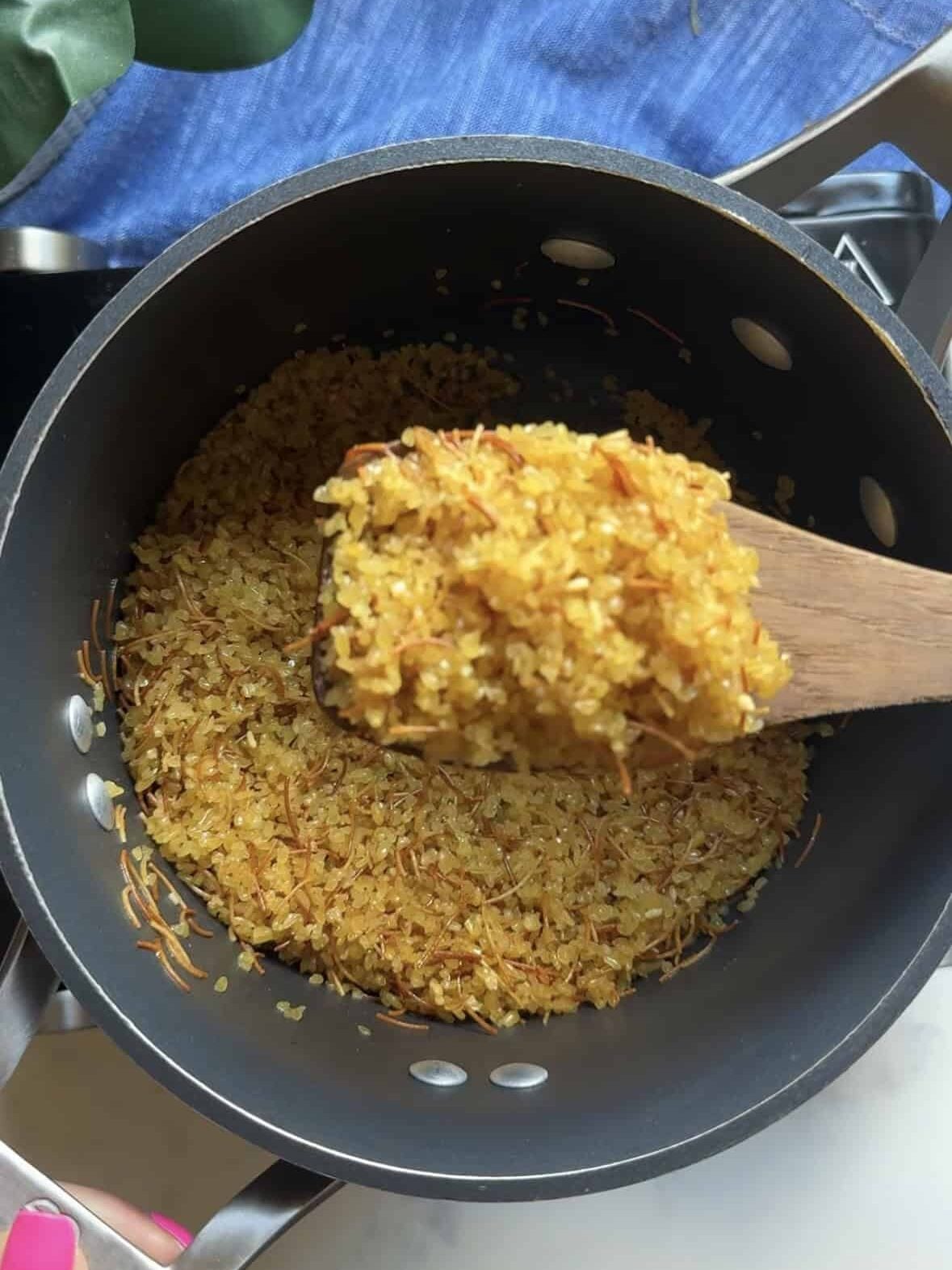 Close up of toasted bulgur and vermicelli lifted with a wooden spoon showing golden color