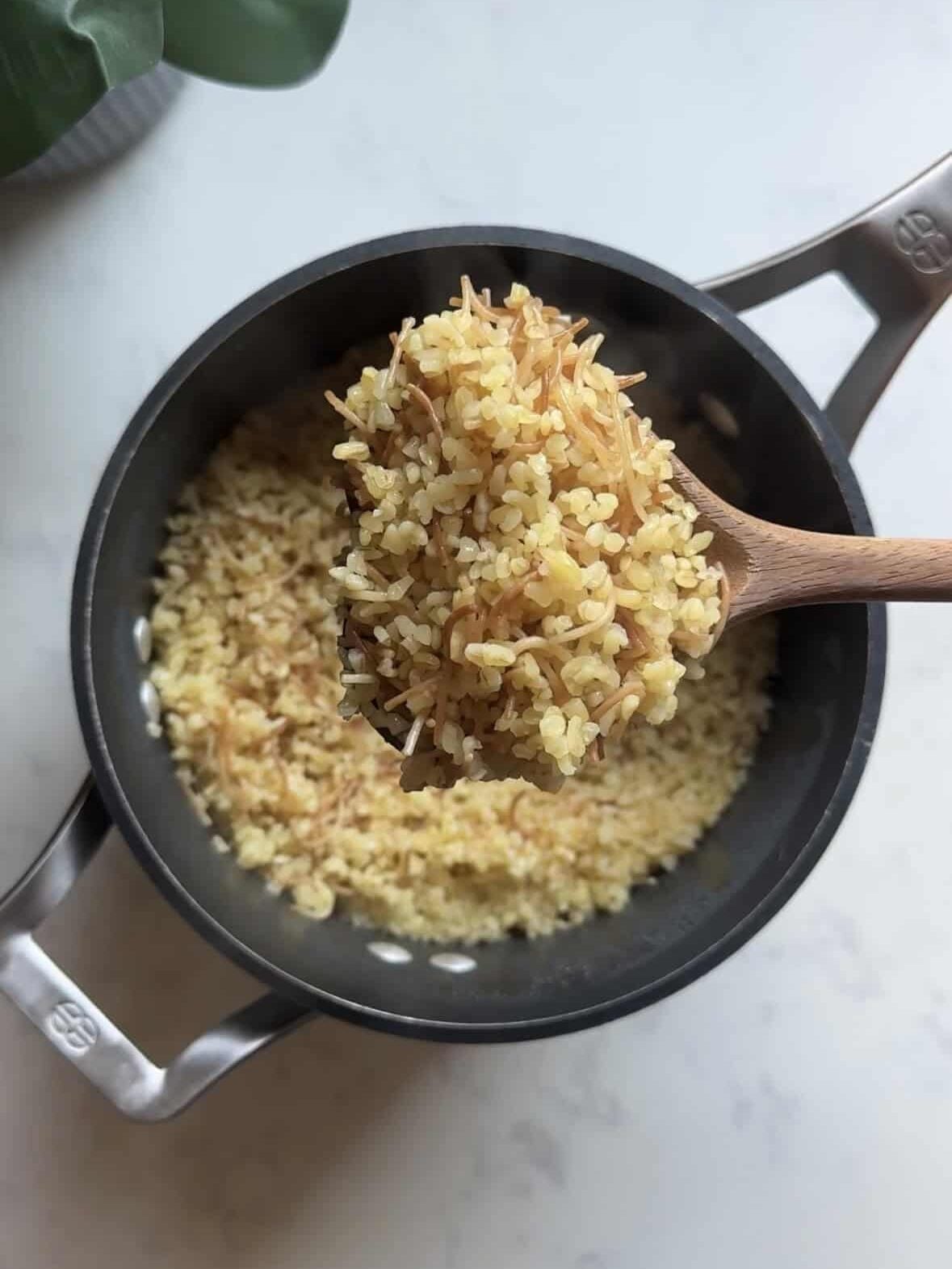Spoon lifting fluffy cooked bulgur pilaf with toasted vermicelli from the pot