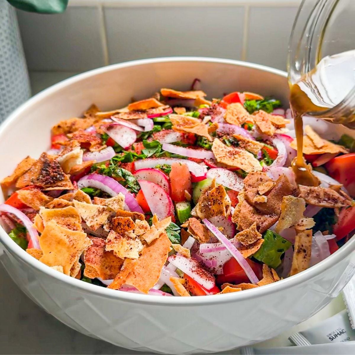 Pouring fattoush dressing over a bowl of fresh vegetables and toasted pita