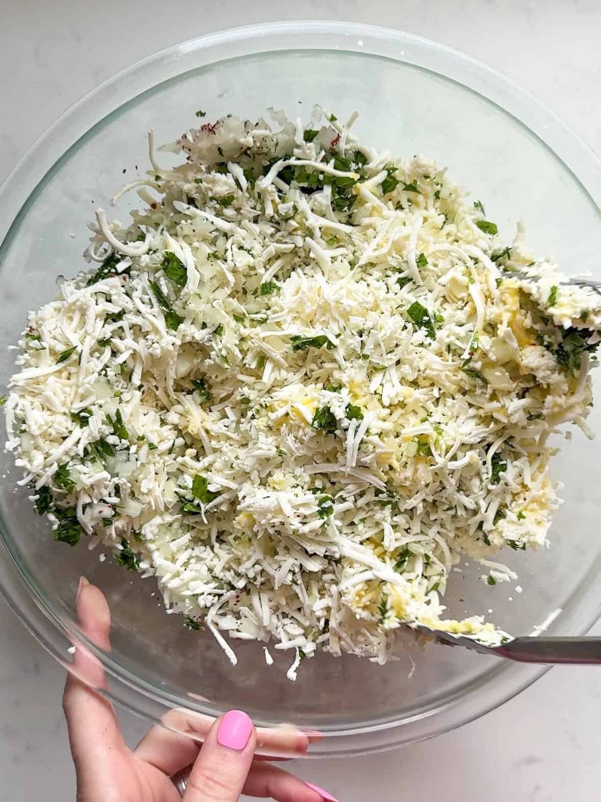 Shredded cheese, parsley, onion, and egg mixed together in a glass bowl for cheese boreg filling