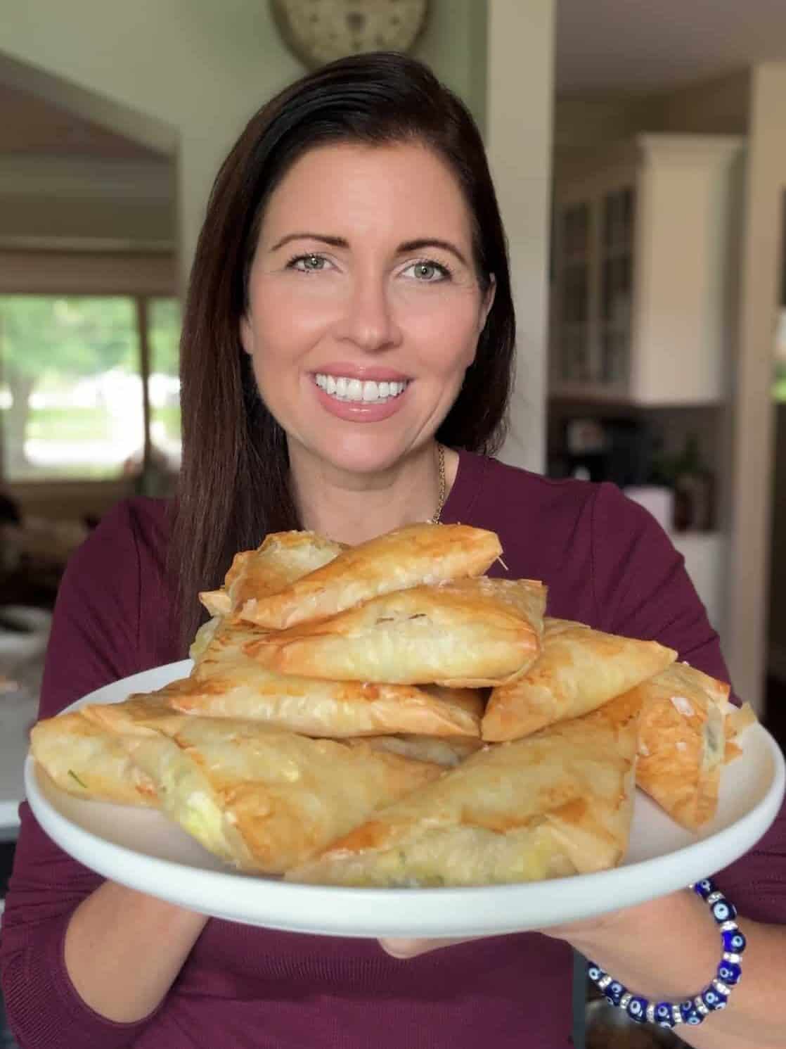 Lindsay from Mom's Dinner Bell smiling and holding a plate of cheese boreg triangles