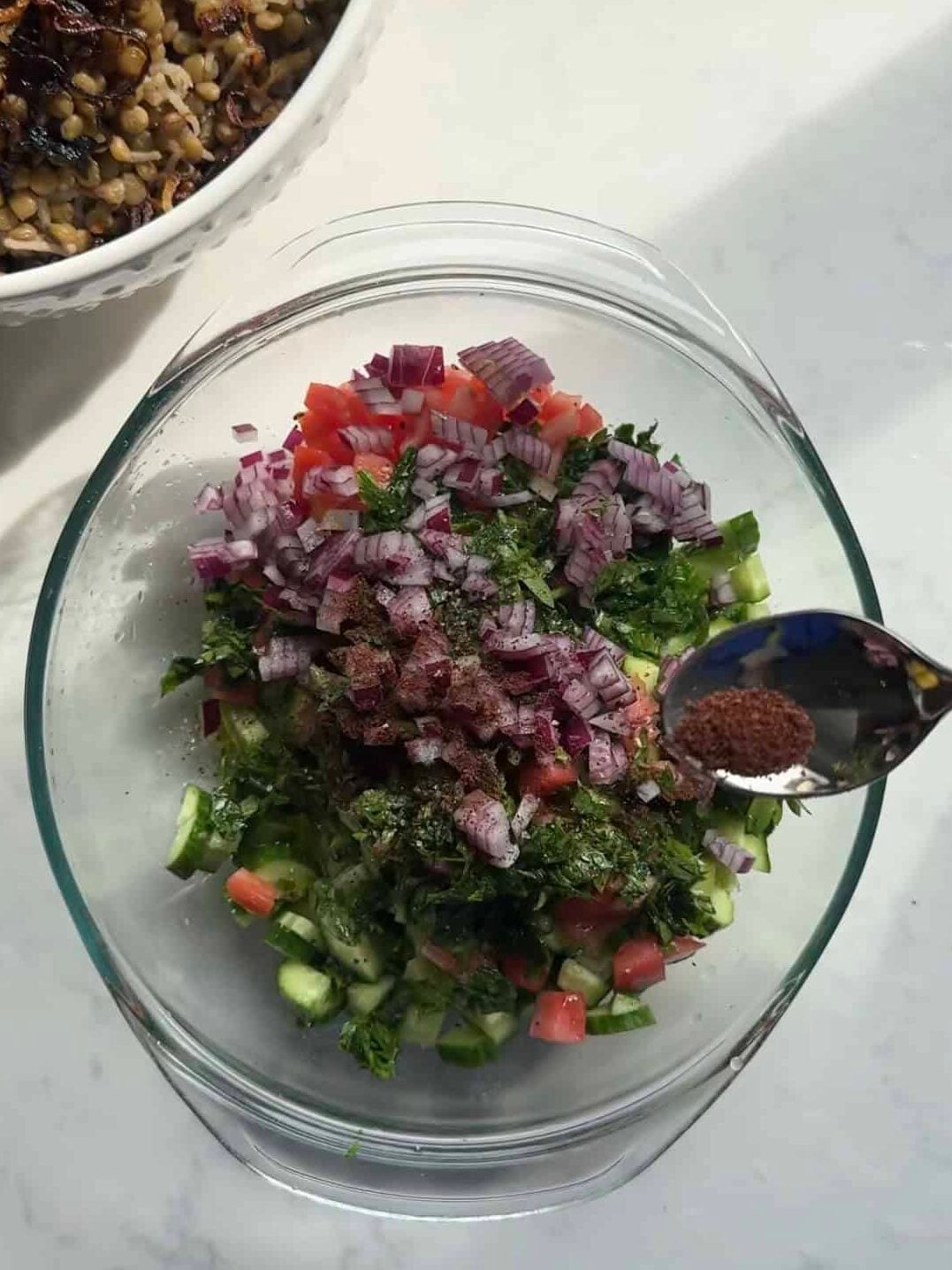 Ground sumac being sprinkled over a bowl of chopped salad with red onion