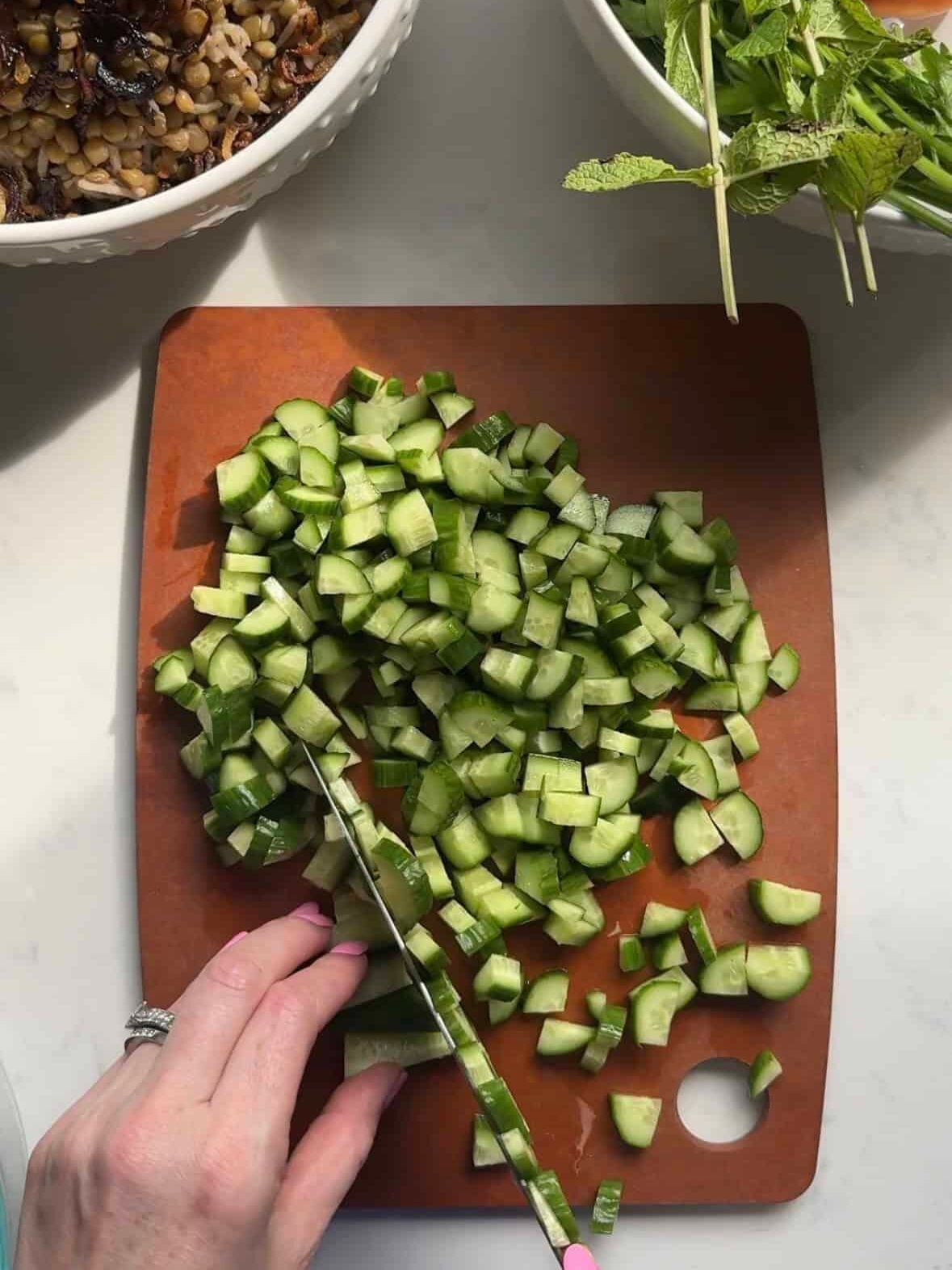 Persian cucumbers being diced on a cutting board for Mediterranean chopped salad