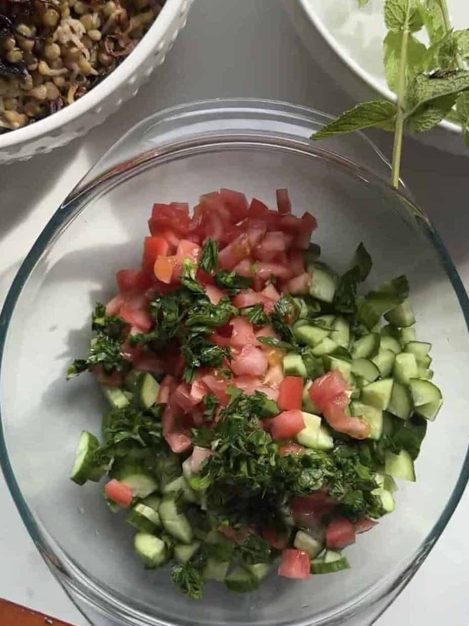 Diced tomato, cucumber, and fresh herbs combined in a glass bowl