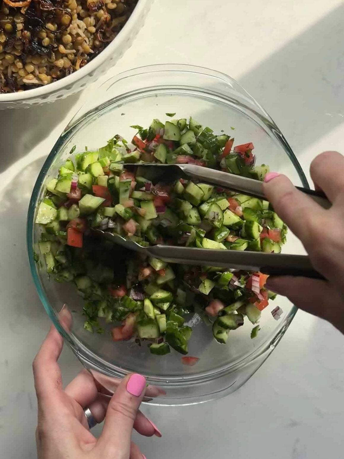 Tossing Mediterranean chopped salad with tongs in a glass bowl