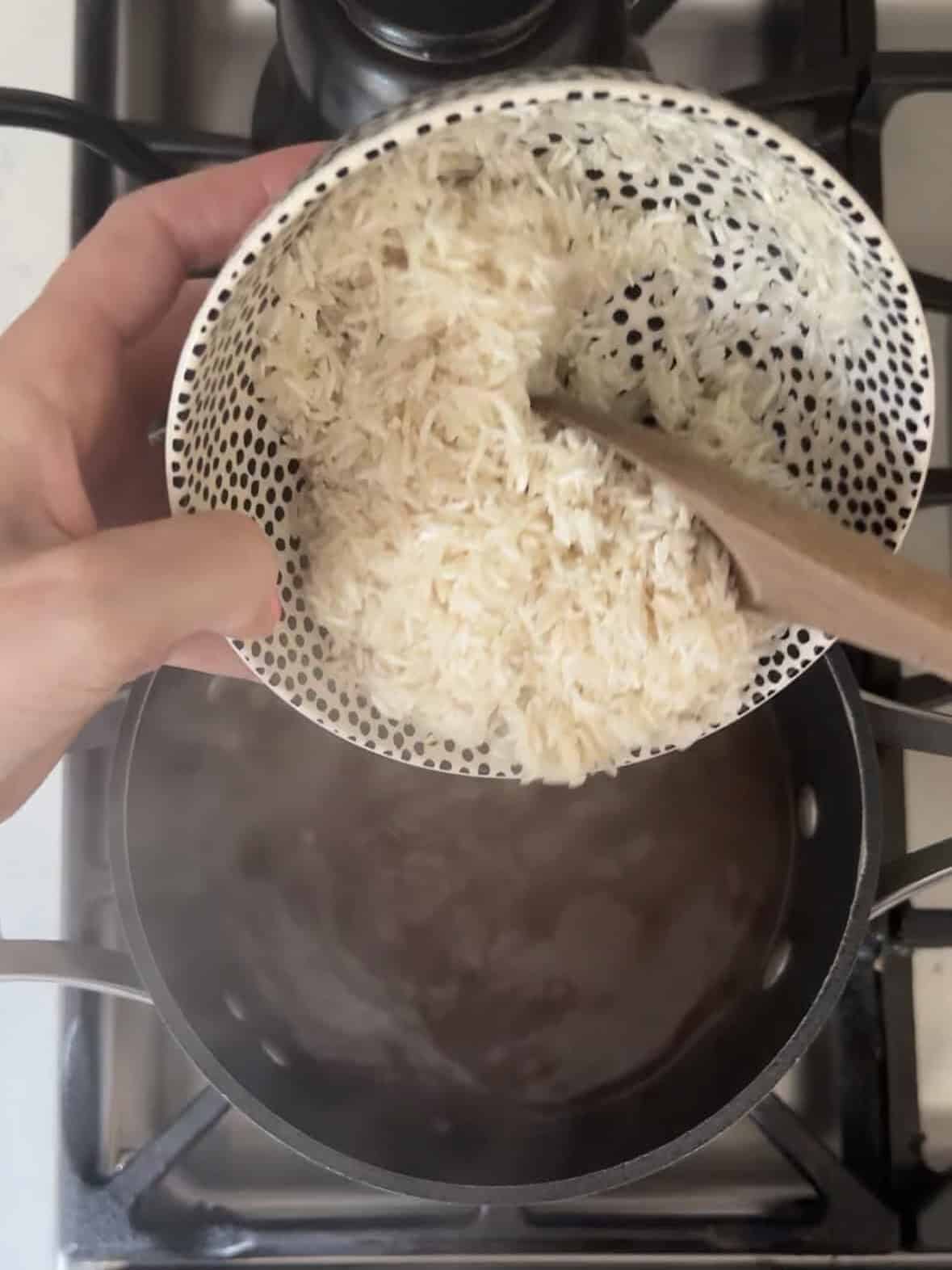 Pouring rinsed basmati rice into a pot on the stove for mujadara