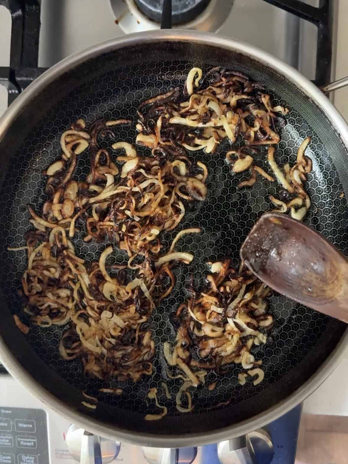 Thinly sliced onions caramelizing in a skillet for mujadara