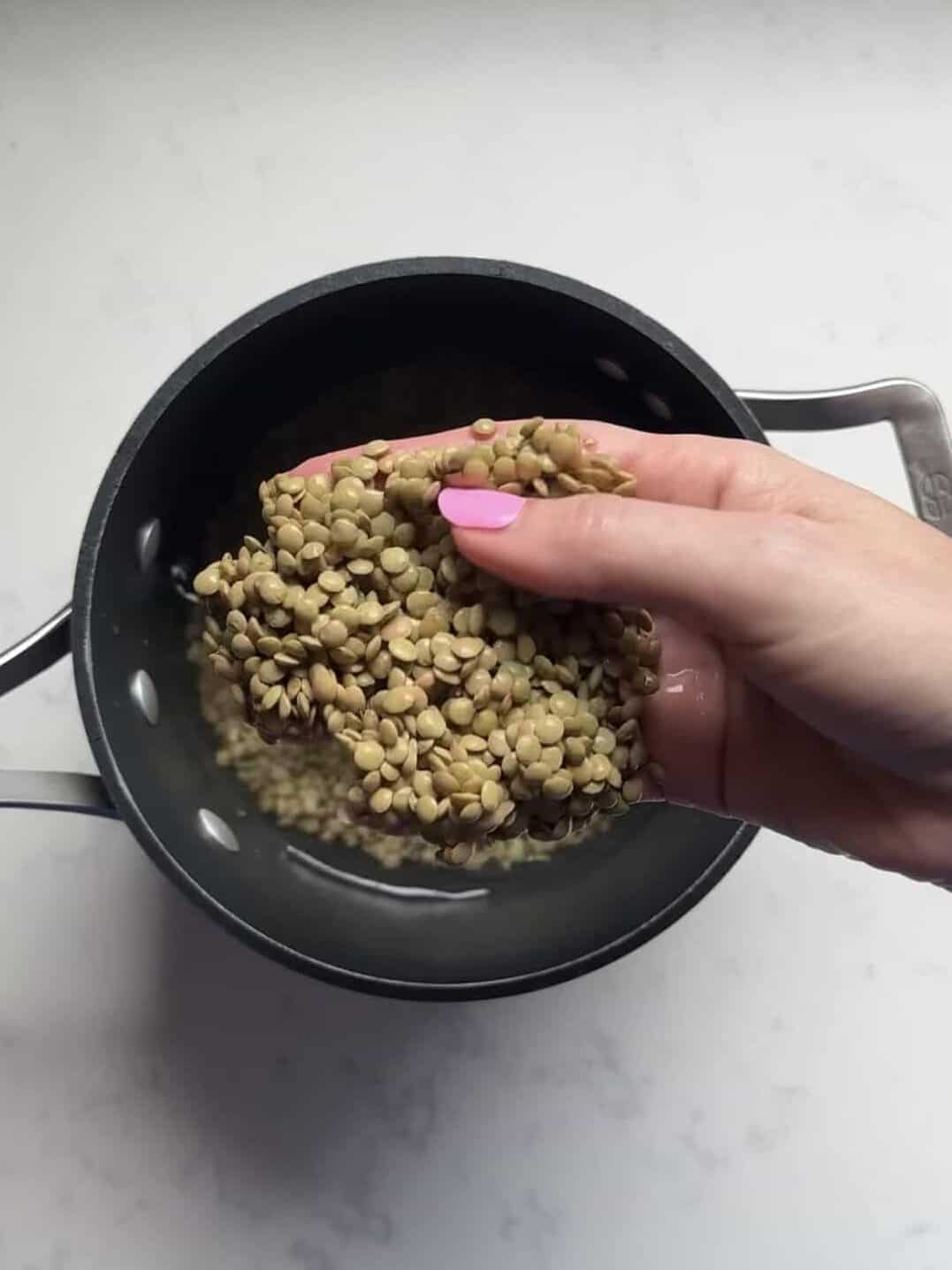 Hand adding rinsed green lentils into a pot to cook for mujadara