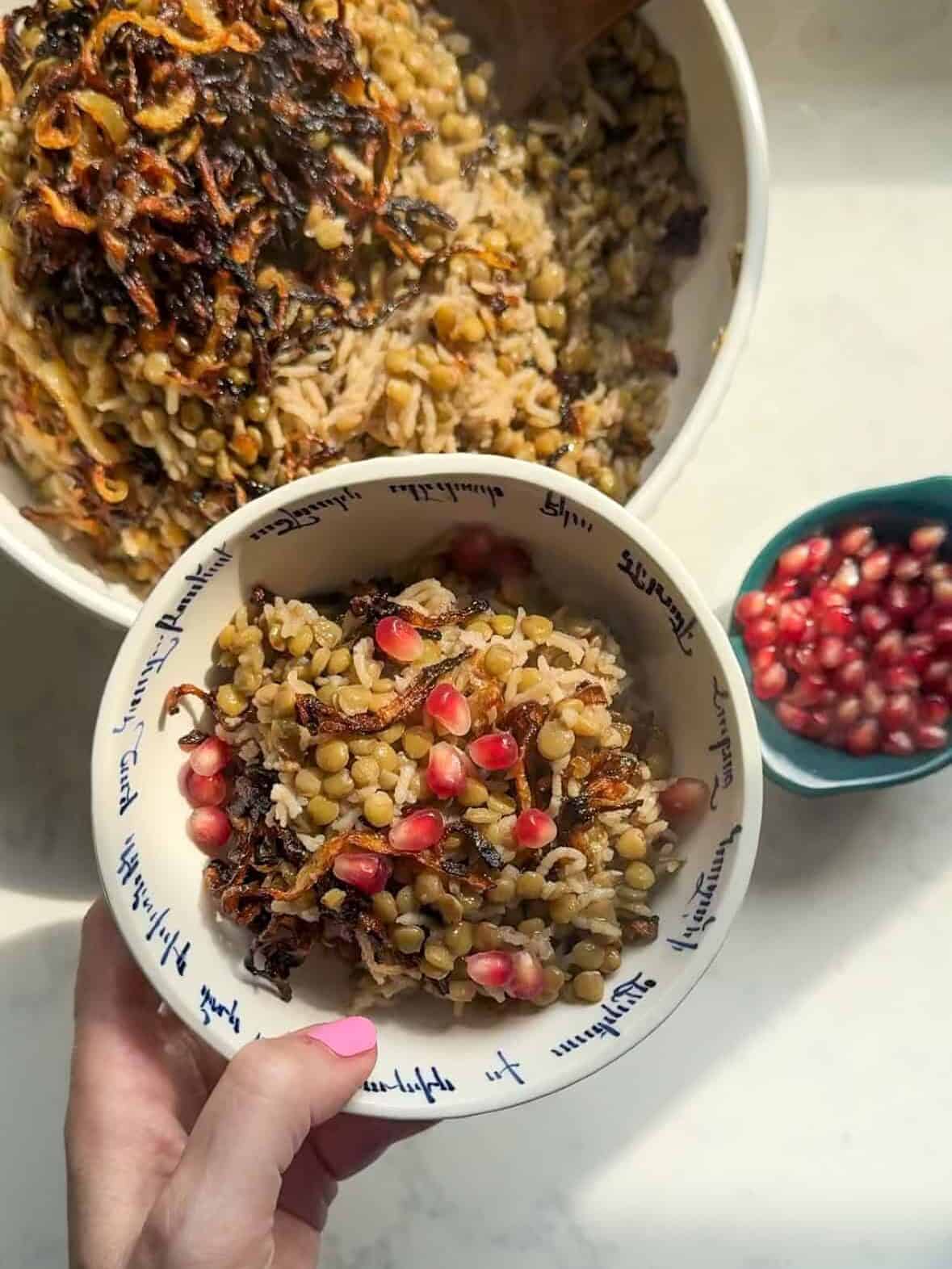 A small bowl of mujadara topped with pomegranate seeds, held in hand