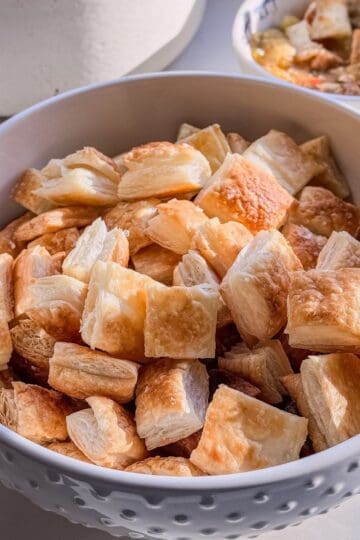 White bowl piled with puff pastry croutons, with a bowl of stew in the background