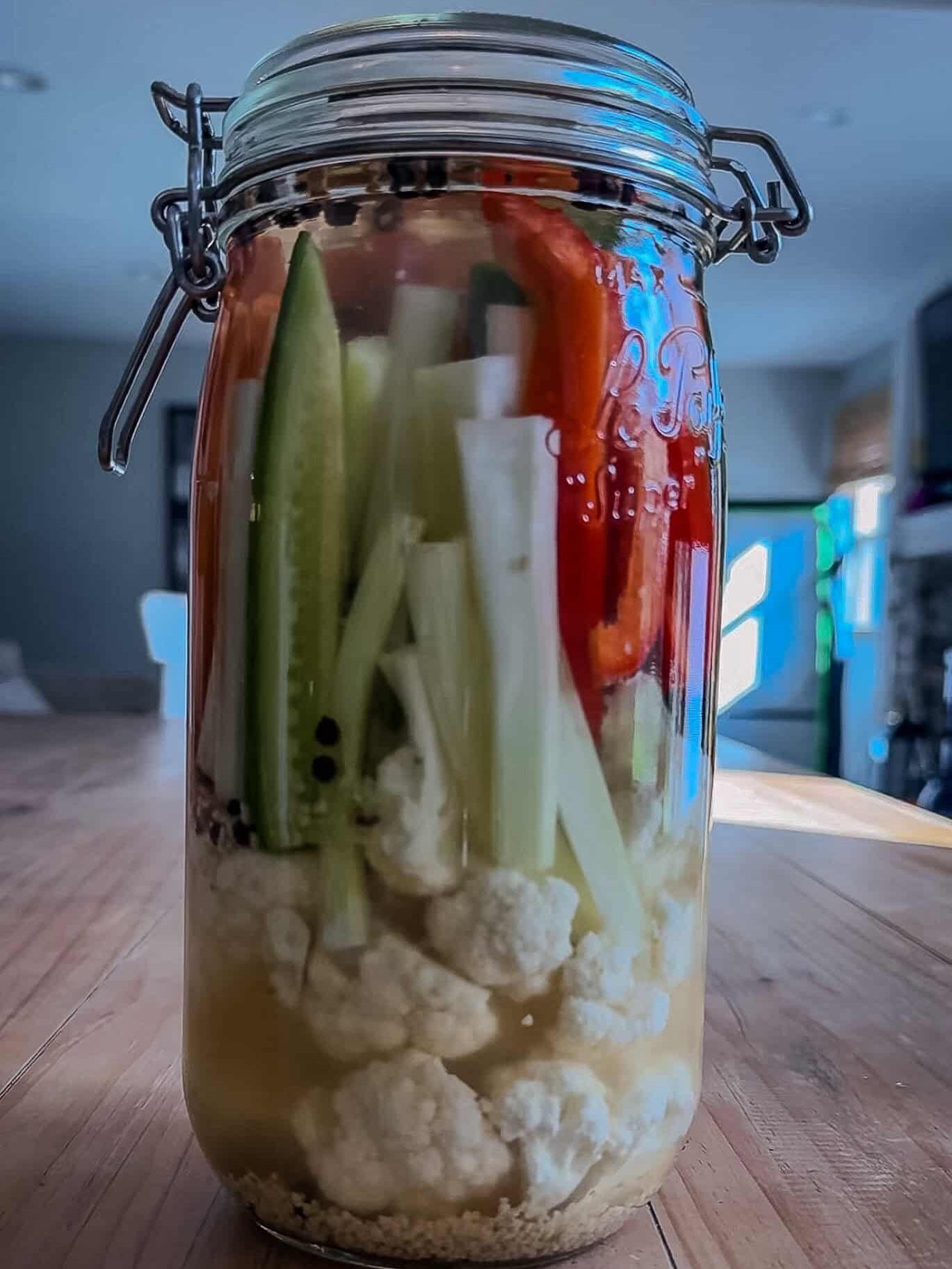 Freshly packed jar of Armenian pickled vegetables in clear brine on a wooden table