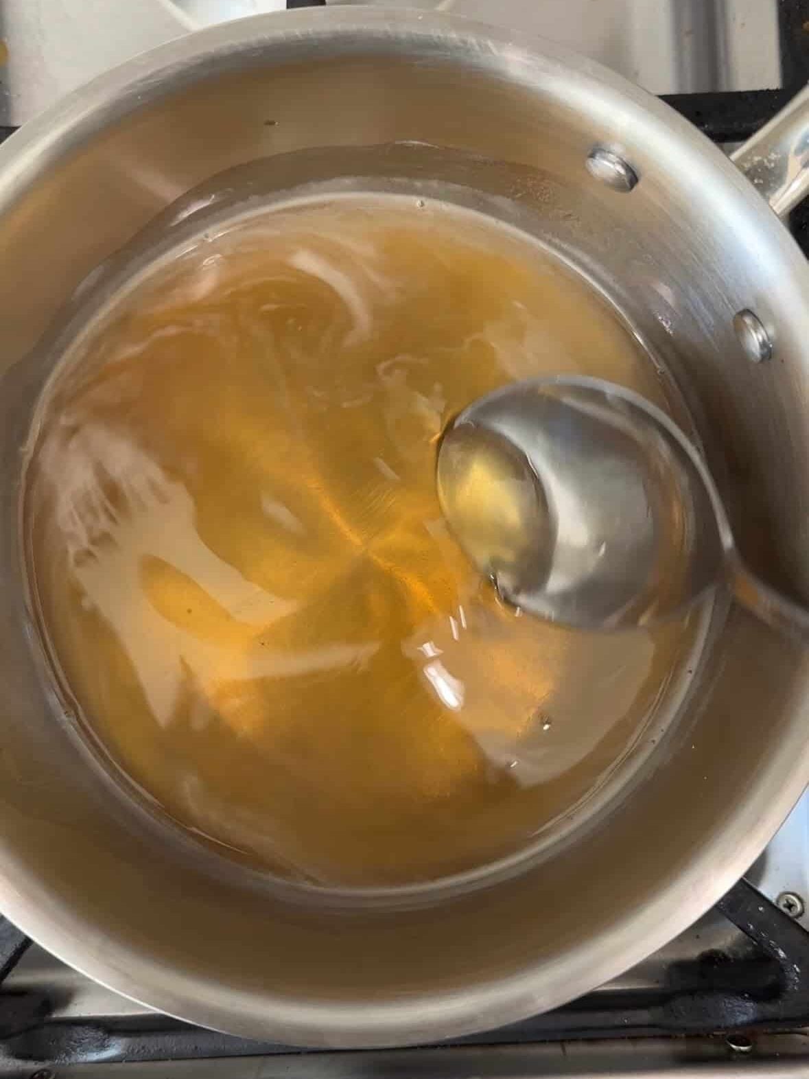 Honey syrup simmering in a stainless steel saucepan with a spoon.
