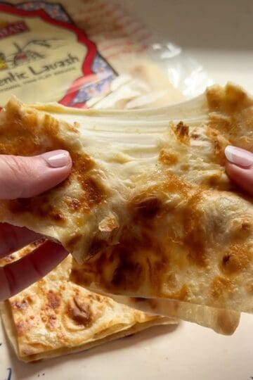 Close-up of a hummus quesadilla pulled apart to show melted Armenian string cheese, with Toufayan lavash in the background.
