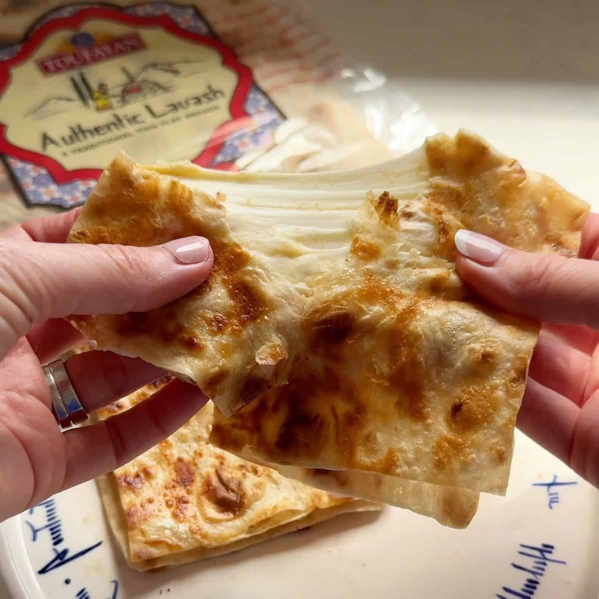 Close-up of a hummus quesadilla pulled apart to show melted Armenian string cheese, with Toufayan lavash in the background.