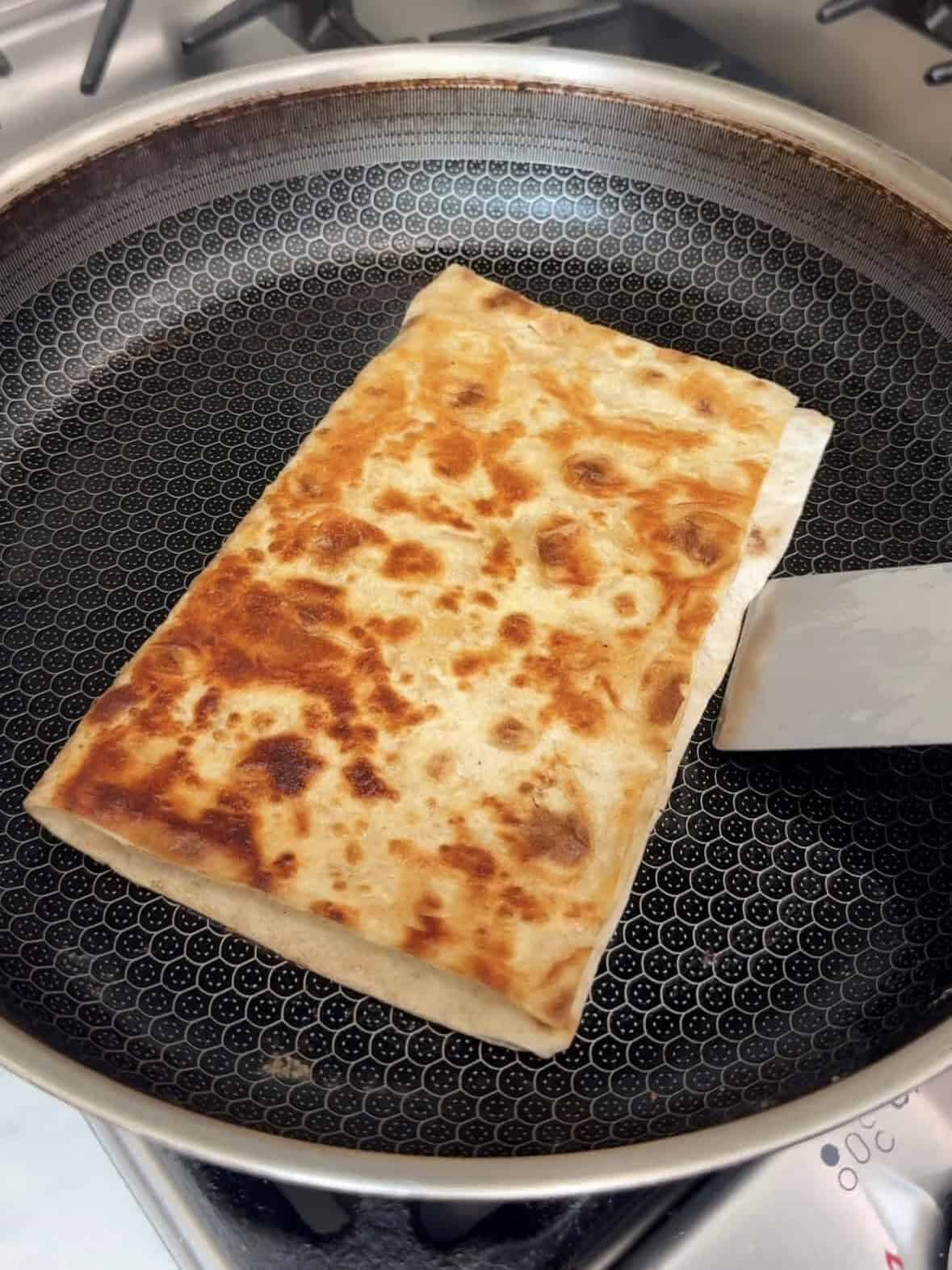 Lavash quesadilla turning golden and crispy in a skillet with a spatula.