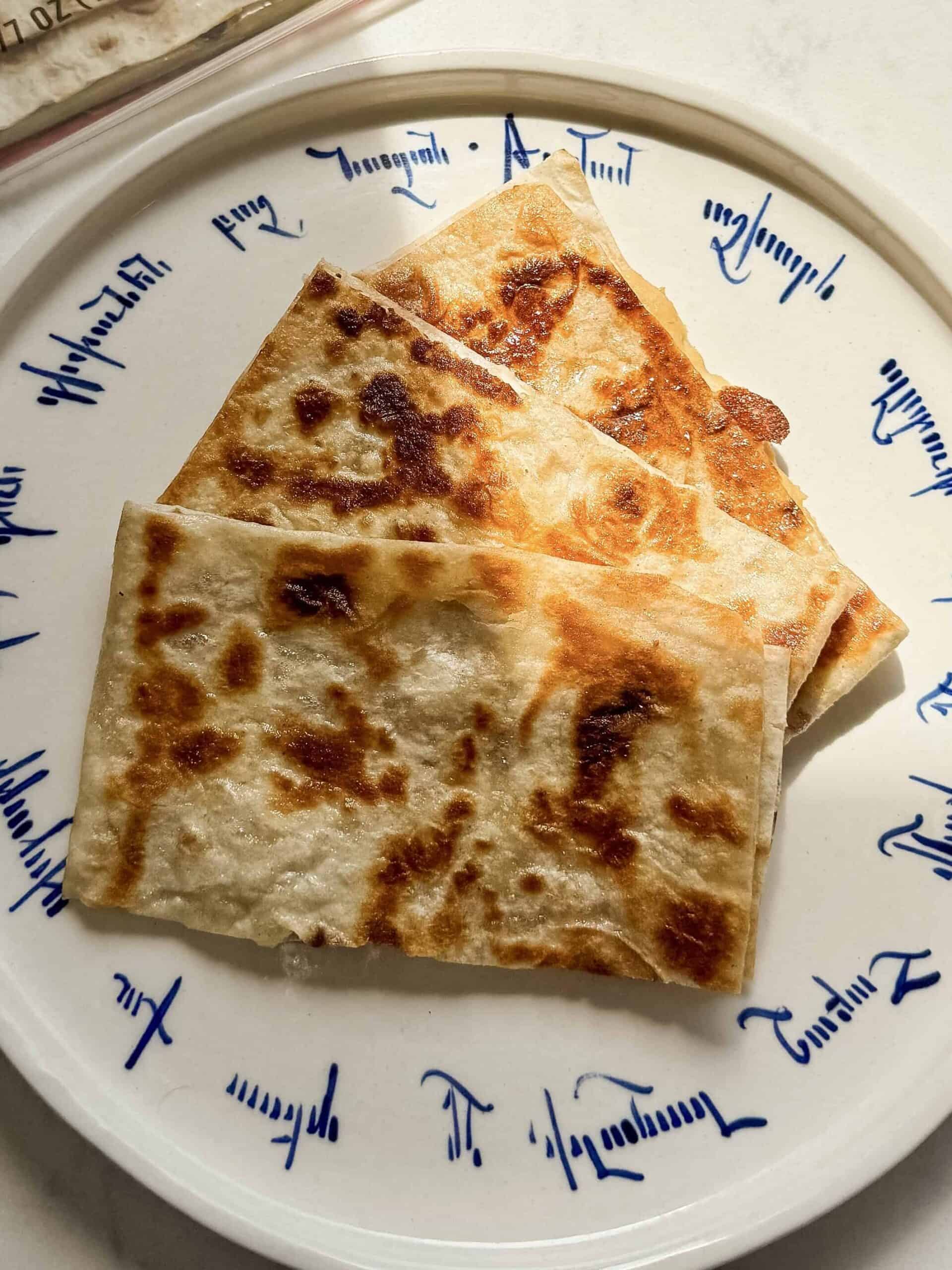 Golden, crispy hummus quesadilla pieces on a plate beside Toufayan lavash.