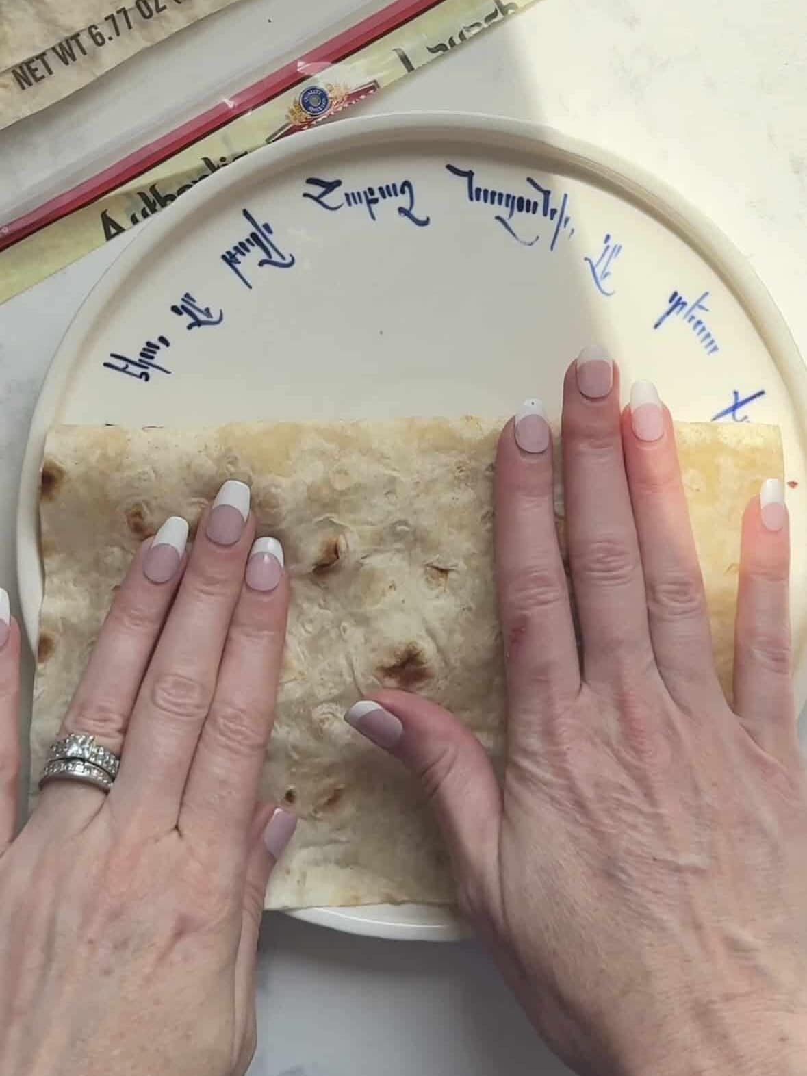 Hands folding a filled sheet of lavash in half on a plate.