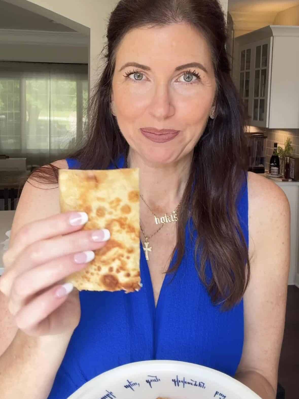 Lindsay from Mom’s Dinner Bell holding a piece of crispy hummus quesadilla in her kitchen.