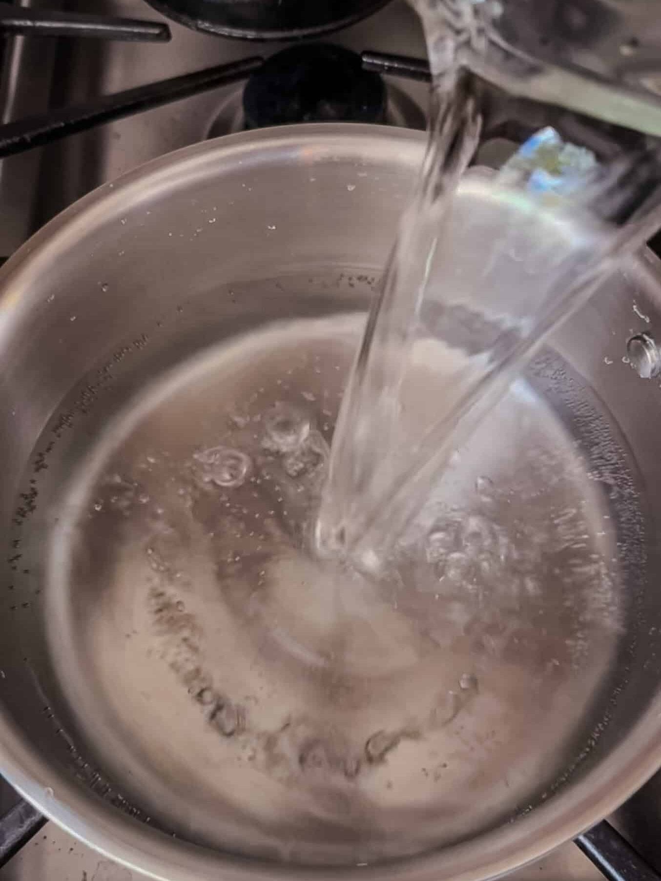 Pouring vinegar into a saucepan of salt water on the stove to make brine for tourshi