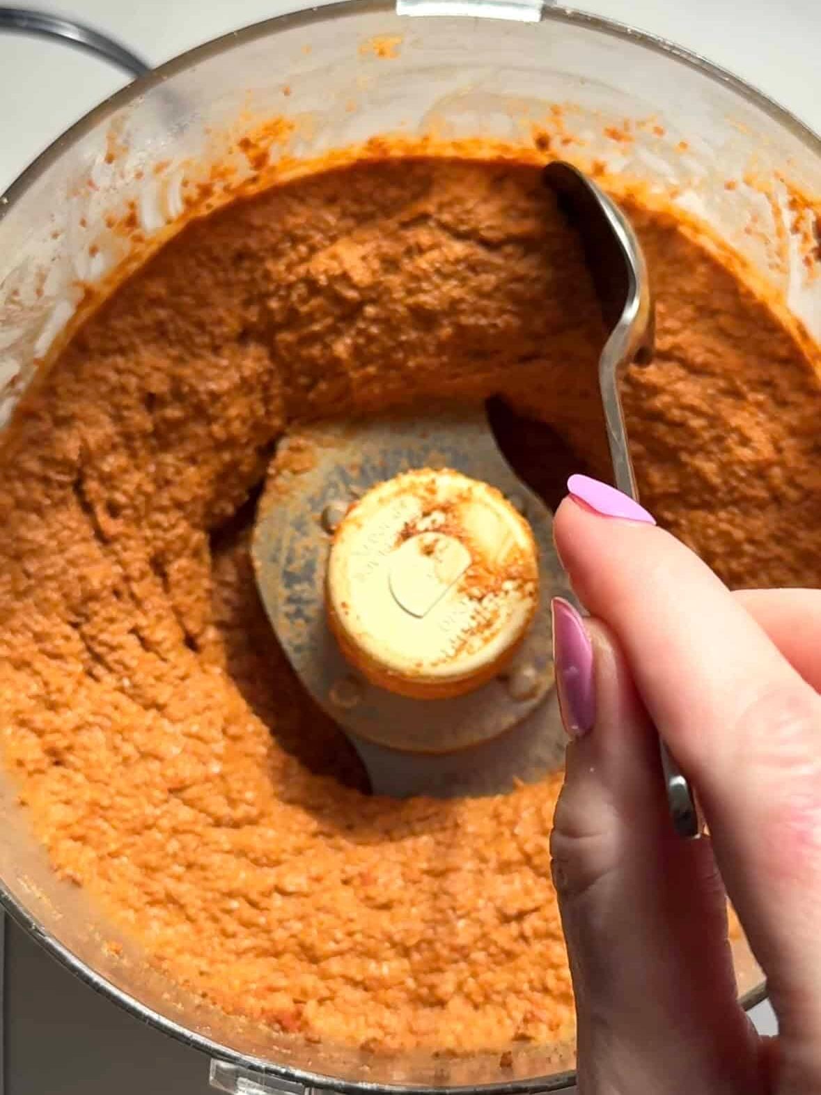 Blended muhammara roasted red pepper and walnut dip in a food processor with a spoon.