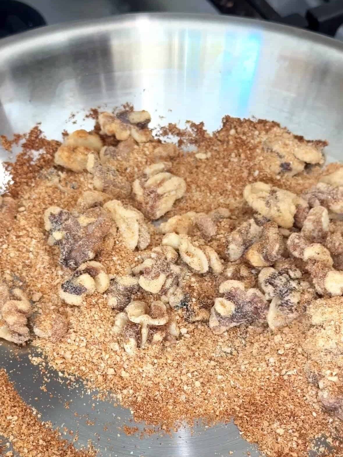 Walnuts and breadcrumbs toasting in a stainless steel skillet.