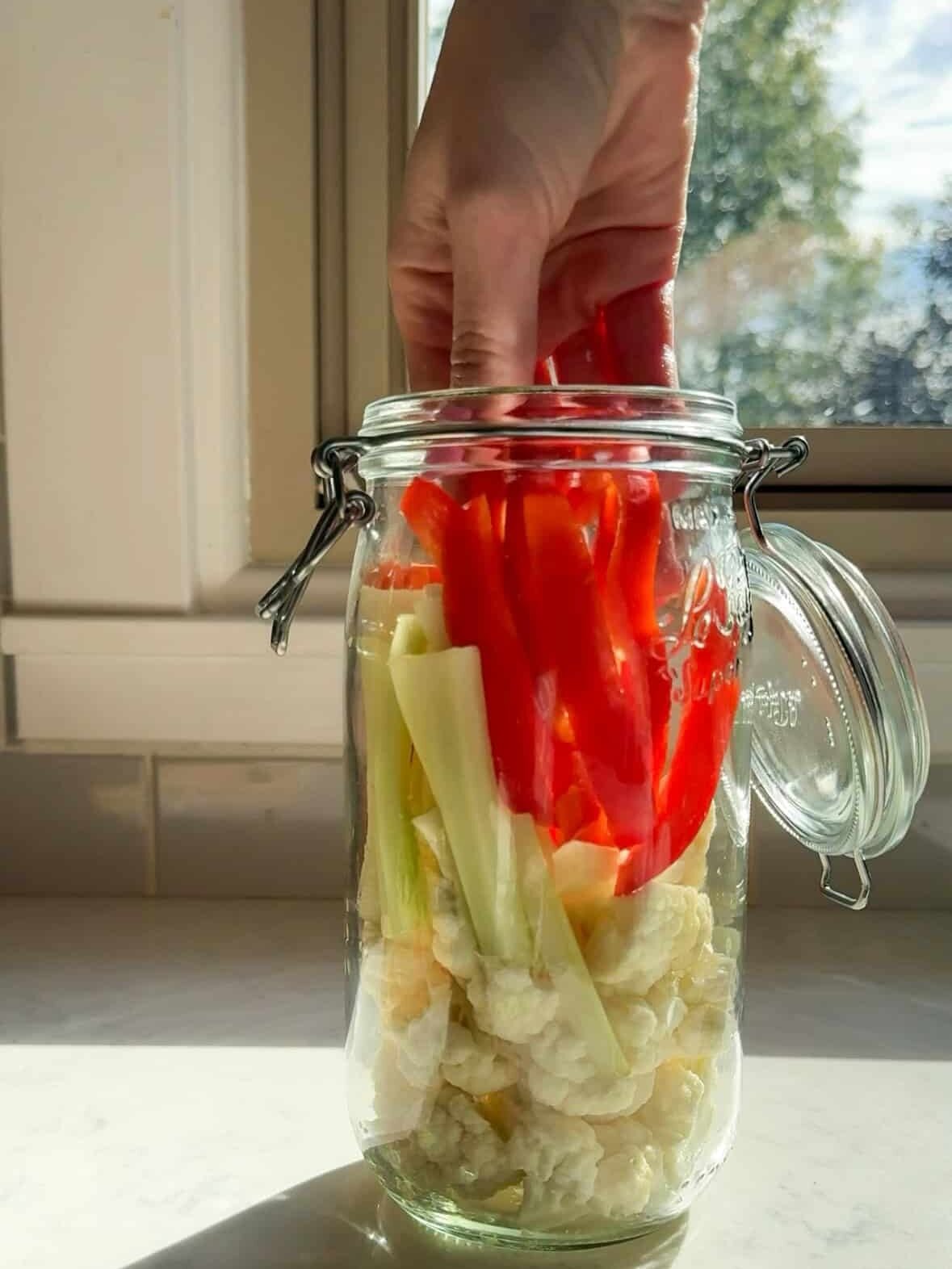 Hand packing red pepper strips into a glass jar with cauliflower and celery for easy pickled vegetables