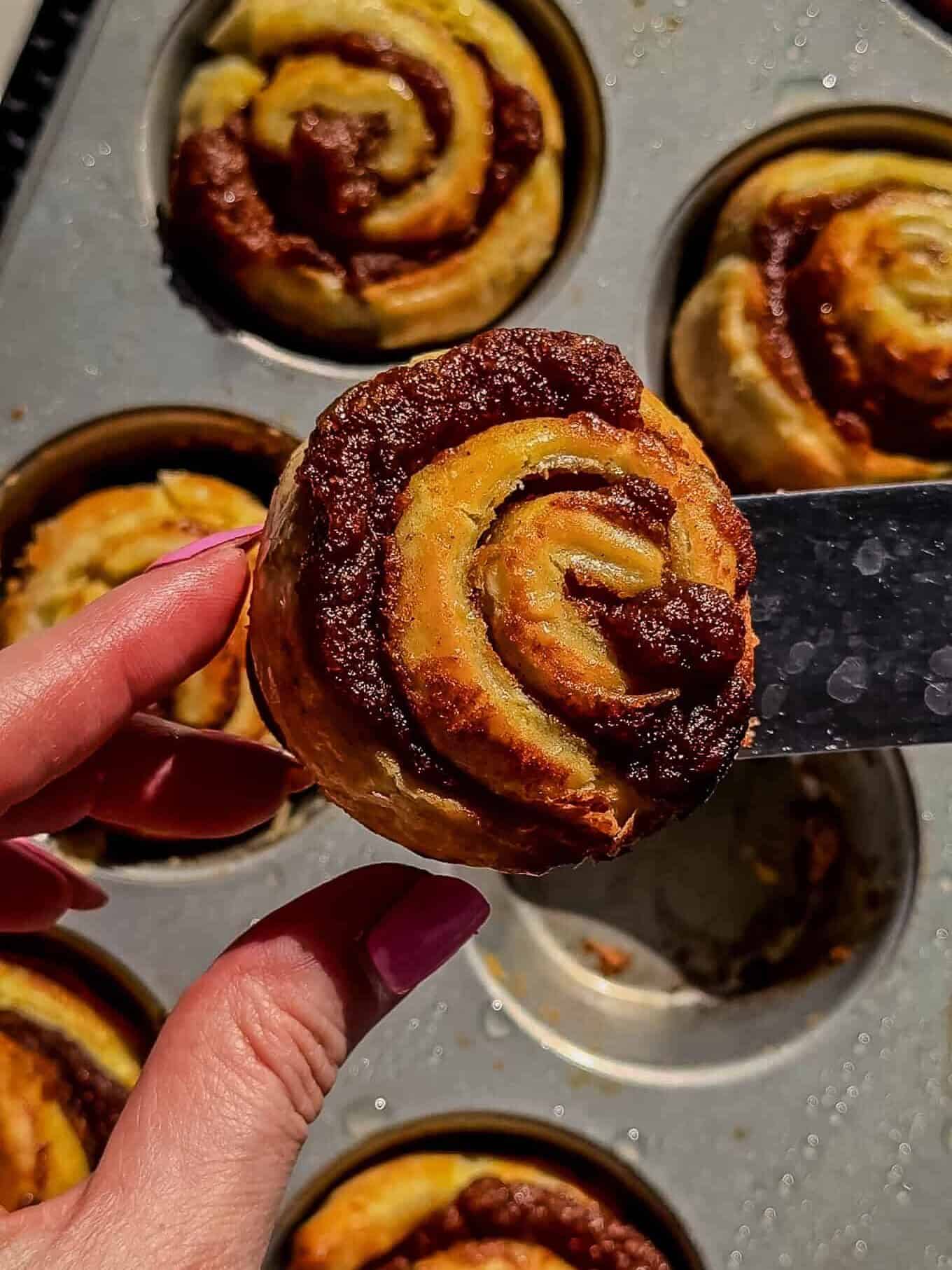 Baked puff pastry pumpkin roll lifted from a muffin tin showing the pumpkin swirl