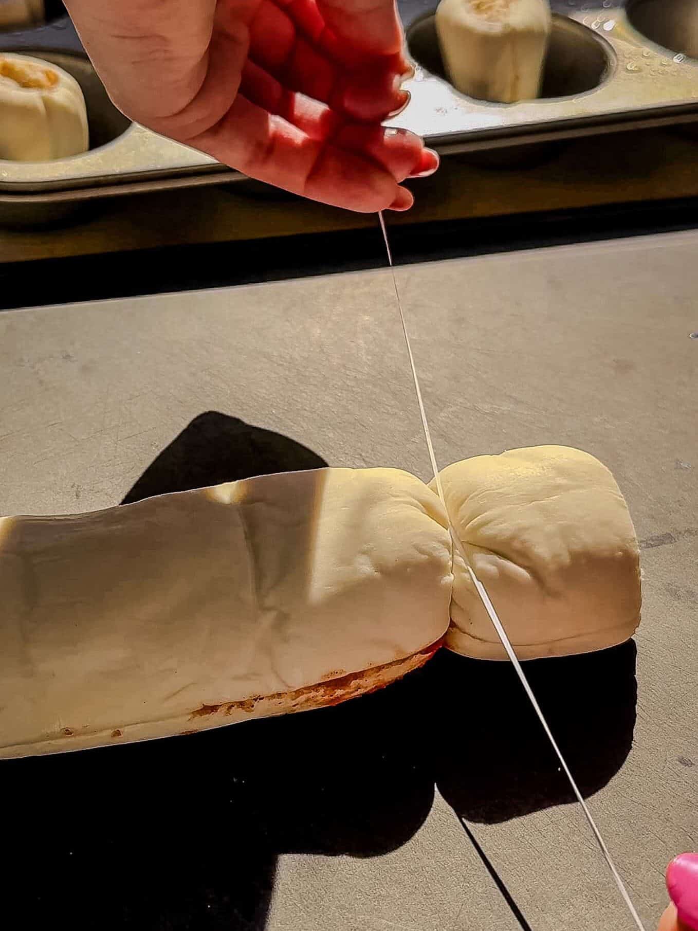 Slicing a puff pastry cinnamon roll log with unflavored dental floss for clean cuts